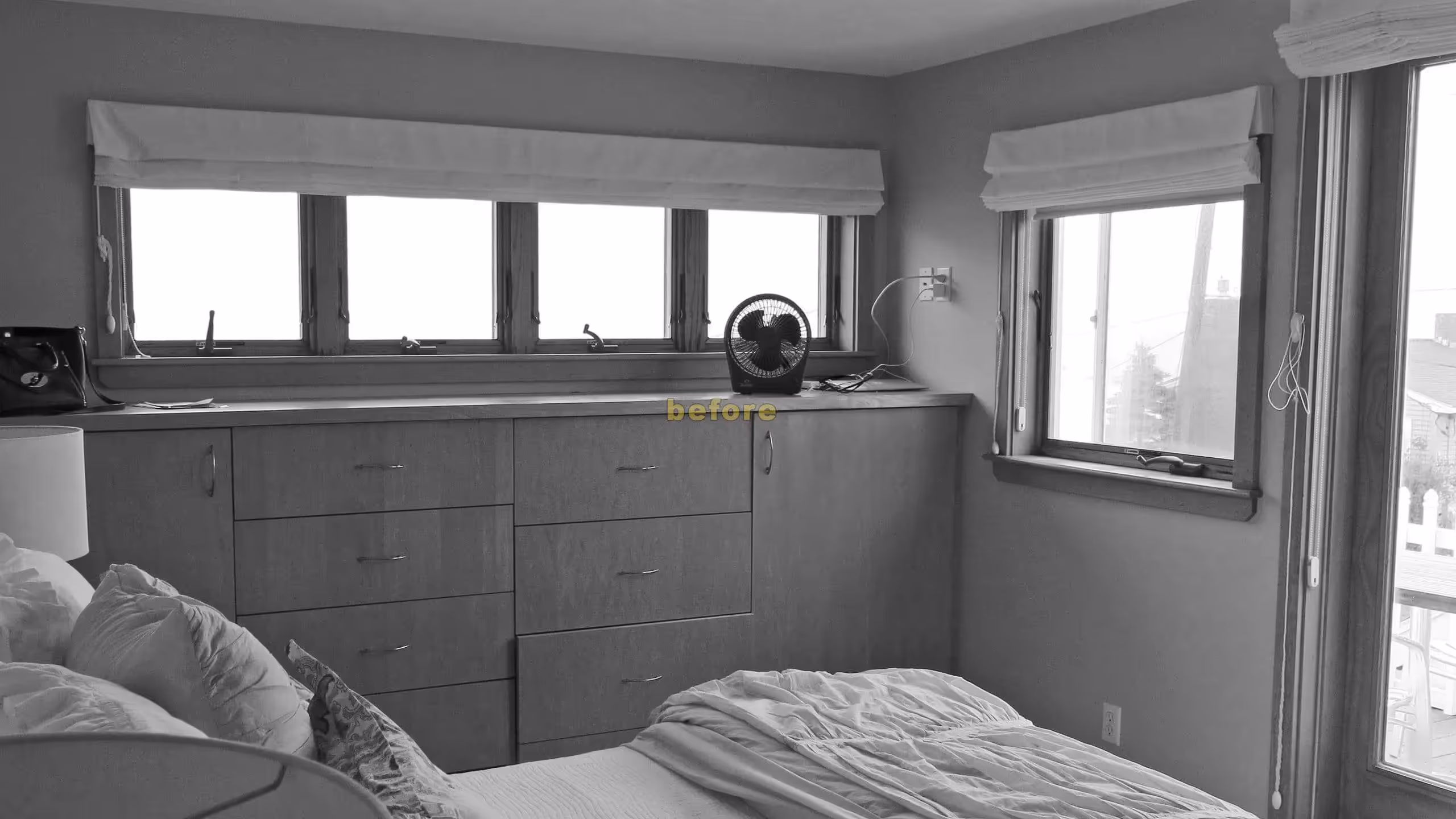 Black and white bedroom with built-in drawers, windows, and unmade bed