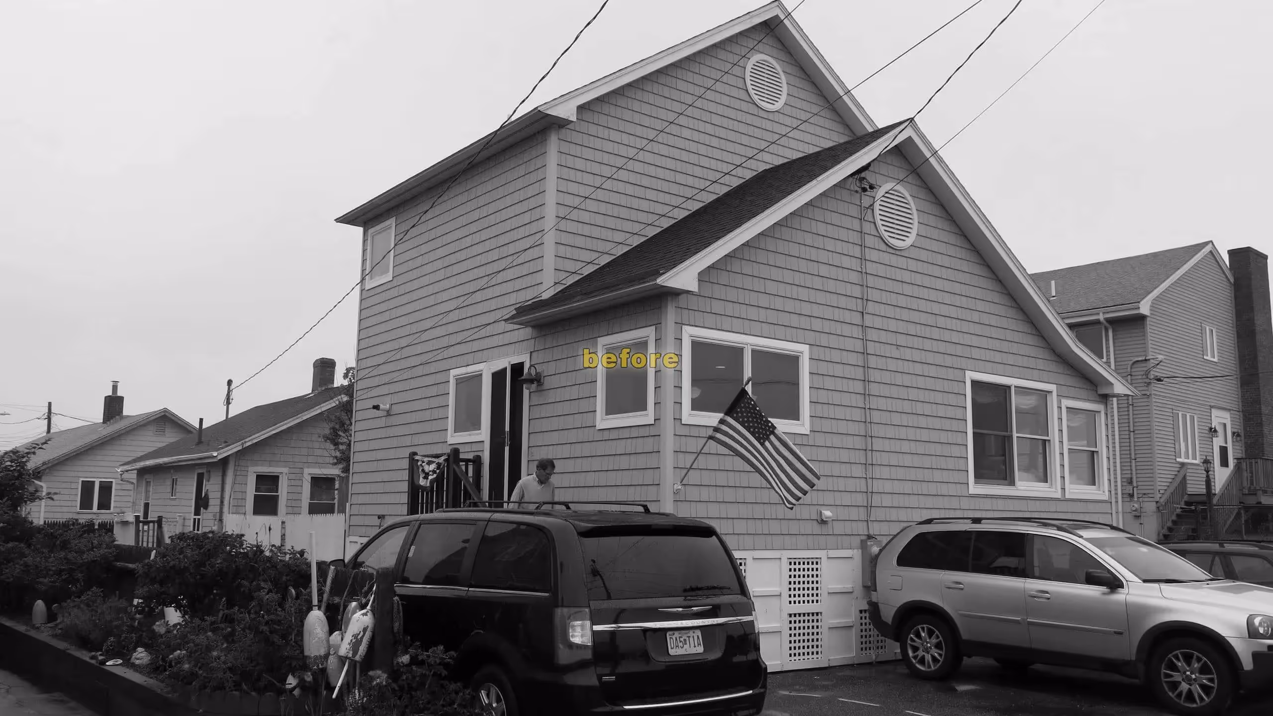 Gray shingled house with American flag, cars parked in driveway