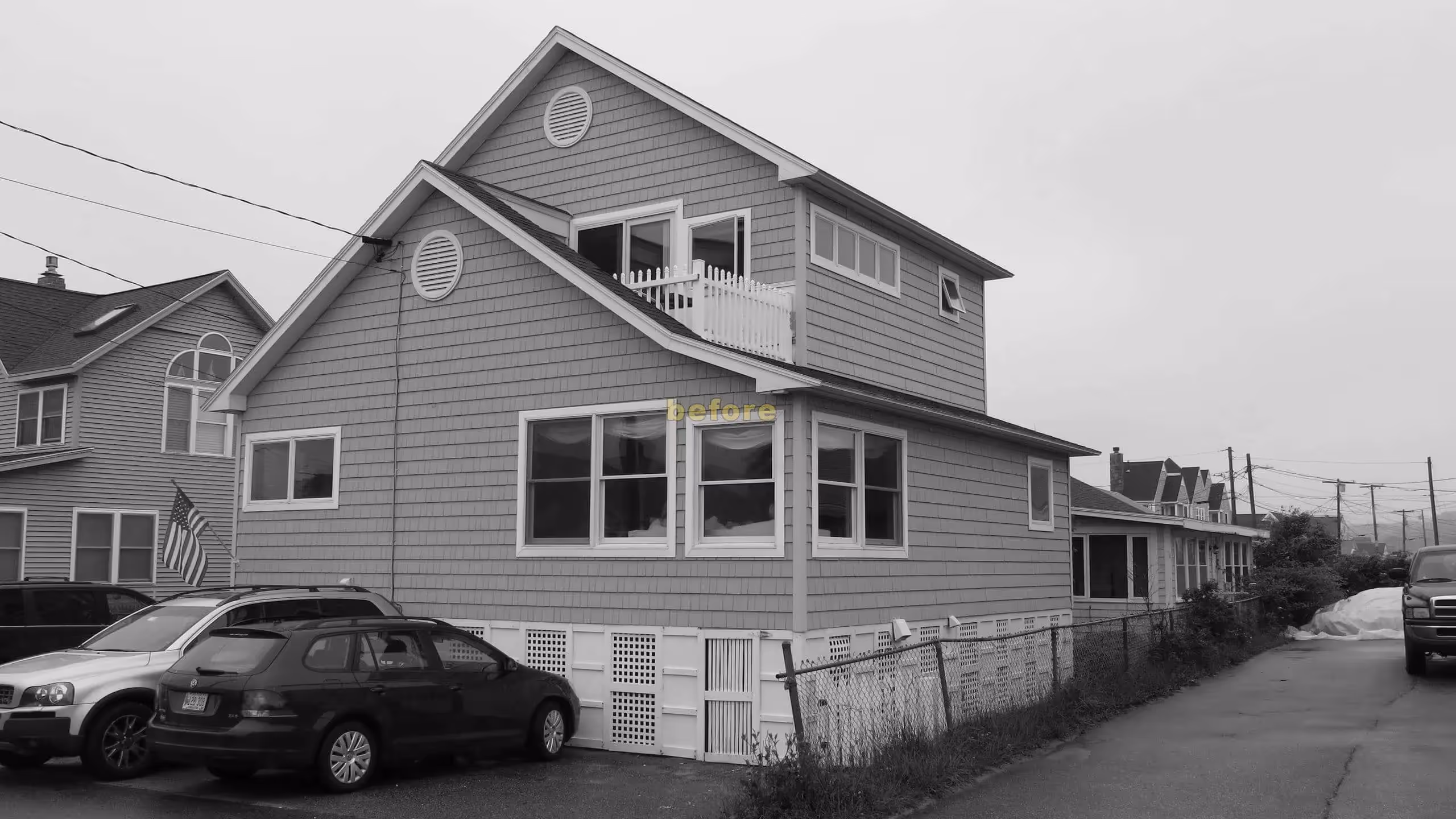 Black and white photo of two-story beach house with cars parked outside