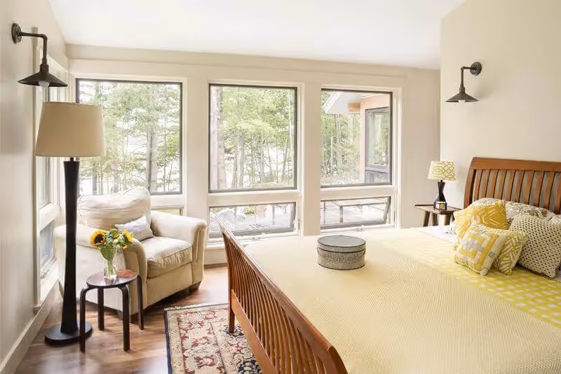 Bright bedroom with large windows, wooden bed, and cozy seating area