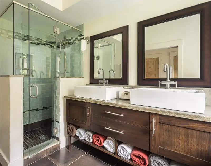 Modern bathroom with glass shower, wooden vanity, and rolled towels
