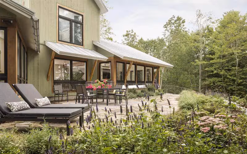 Modern cabin with garden patio surrounded by lush green forest and flowering plants