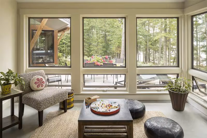 Cozy sunroom with large windows overlooking forest and outdoor deck