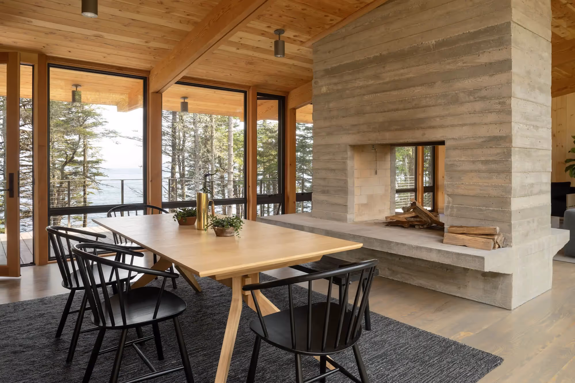 Wooden dining area with forest and ocean view, modern fireplace