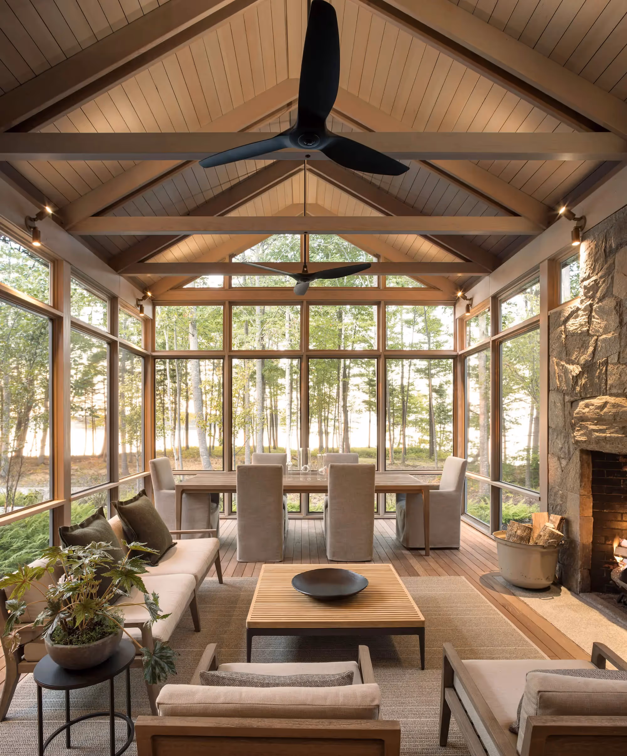 Modern sunroom with glass walls, dining area, and forest view