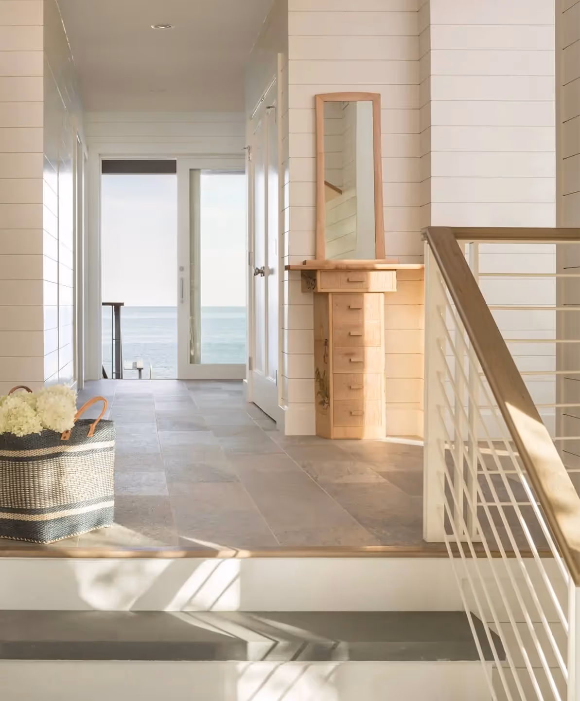 Bright coastal hallway with ocean view, wooden furniture, and white railings