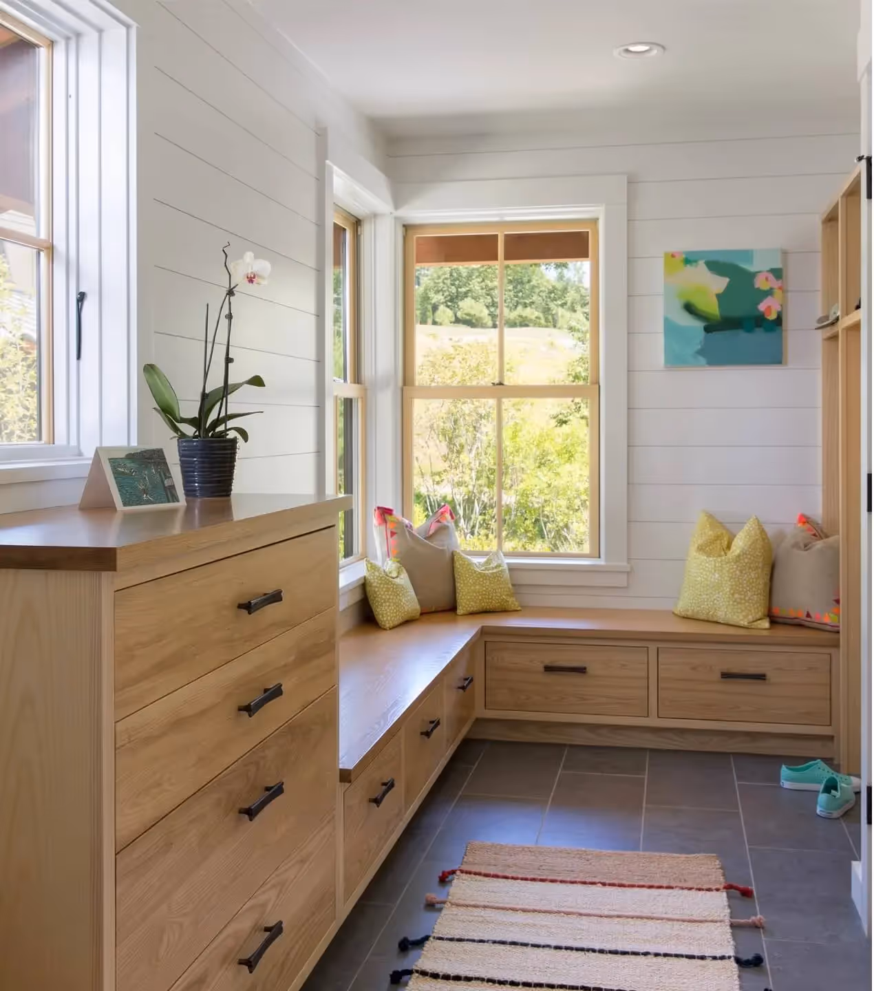 Bright mudroom with wooden cabinets, window seat, and potted orchid