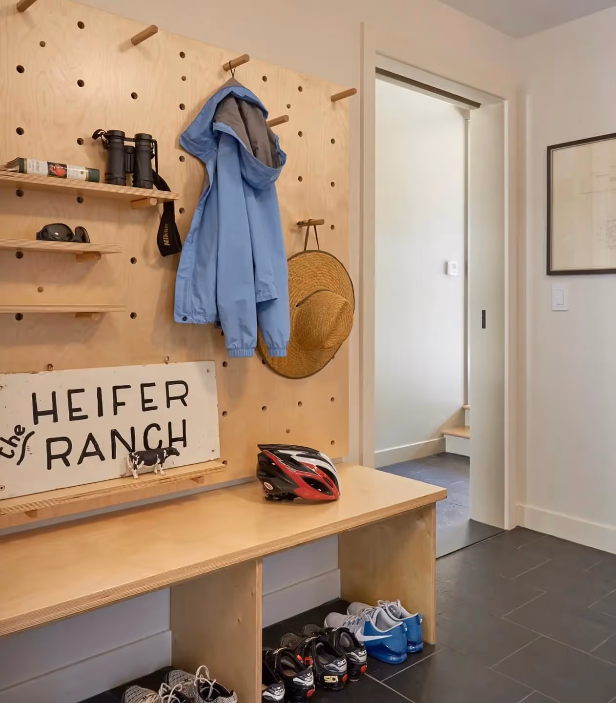 Mudroom with pegboard, blue jacket, straw hat, bike helmet, and Heifer Ranch sign