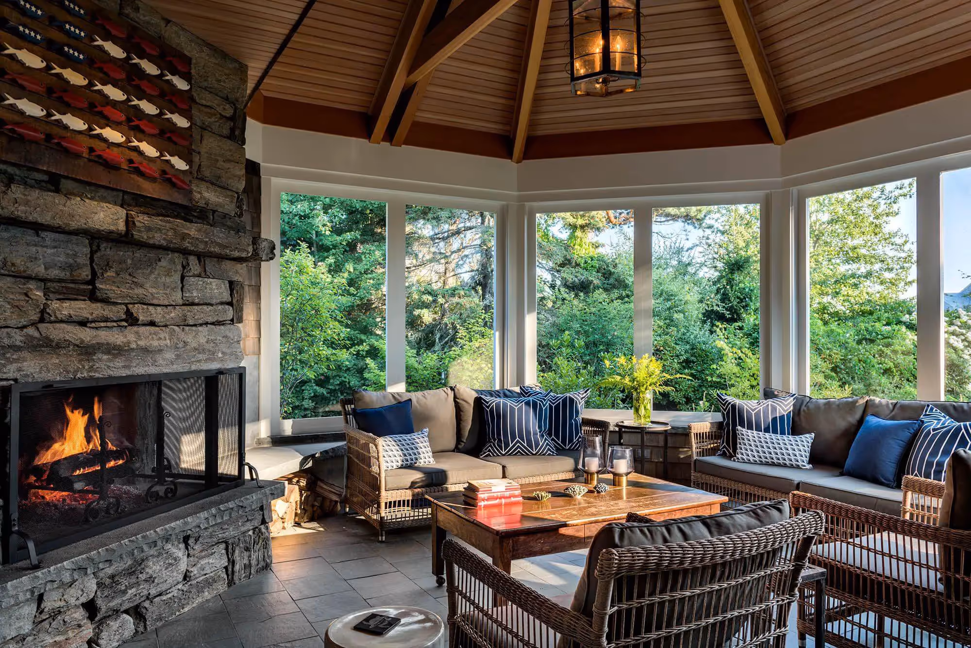 Cozy sunroom with fireplace, wicker furniture, and forest view through large windows