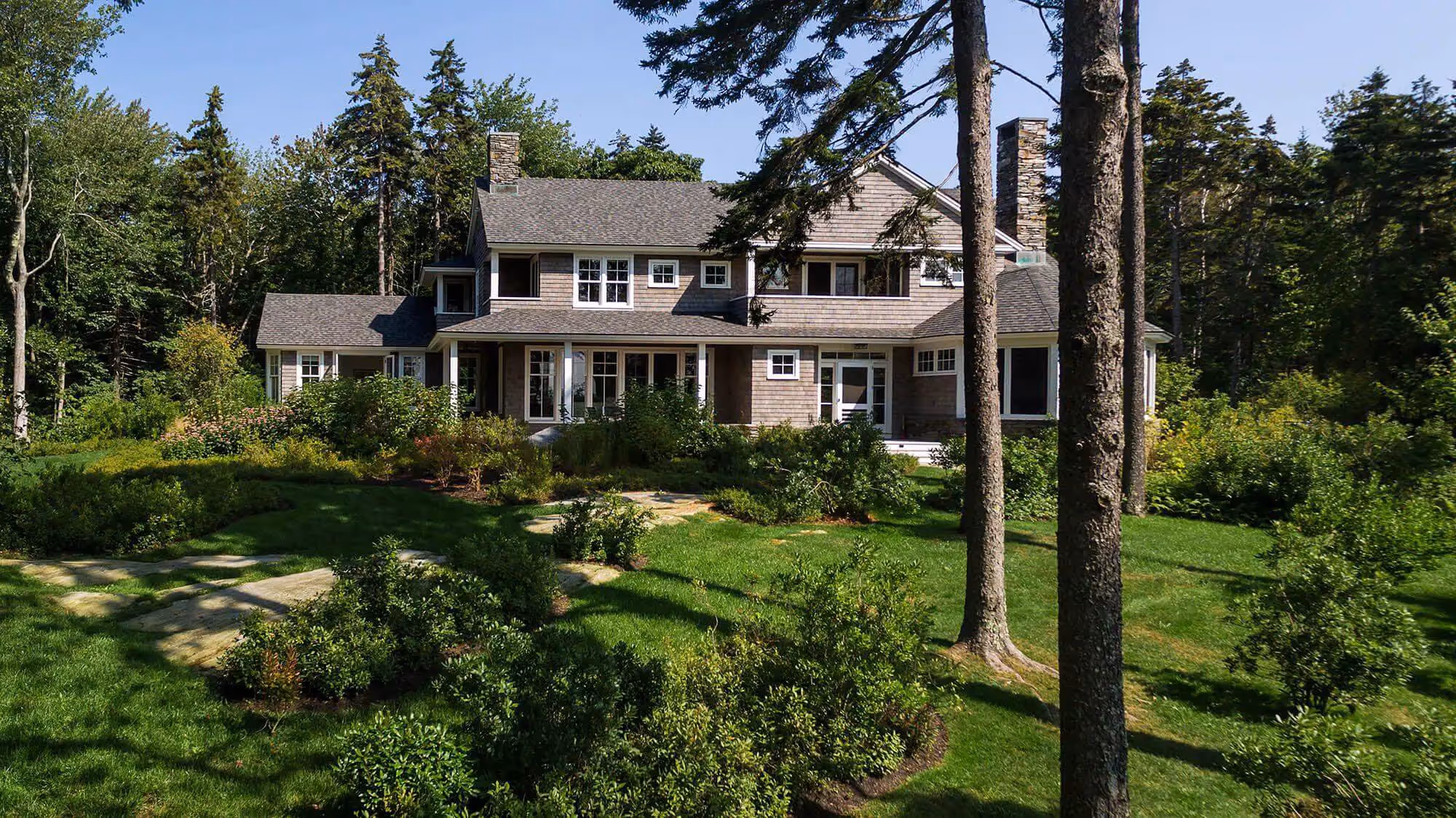 Large two-story house nestled in lush forest with manicured green lawn