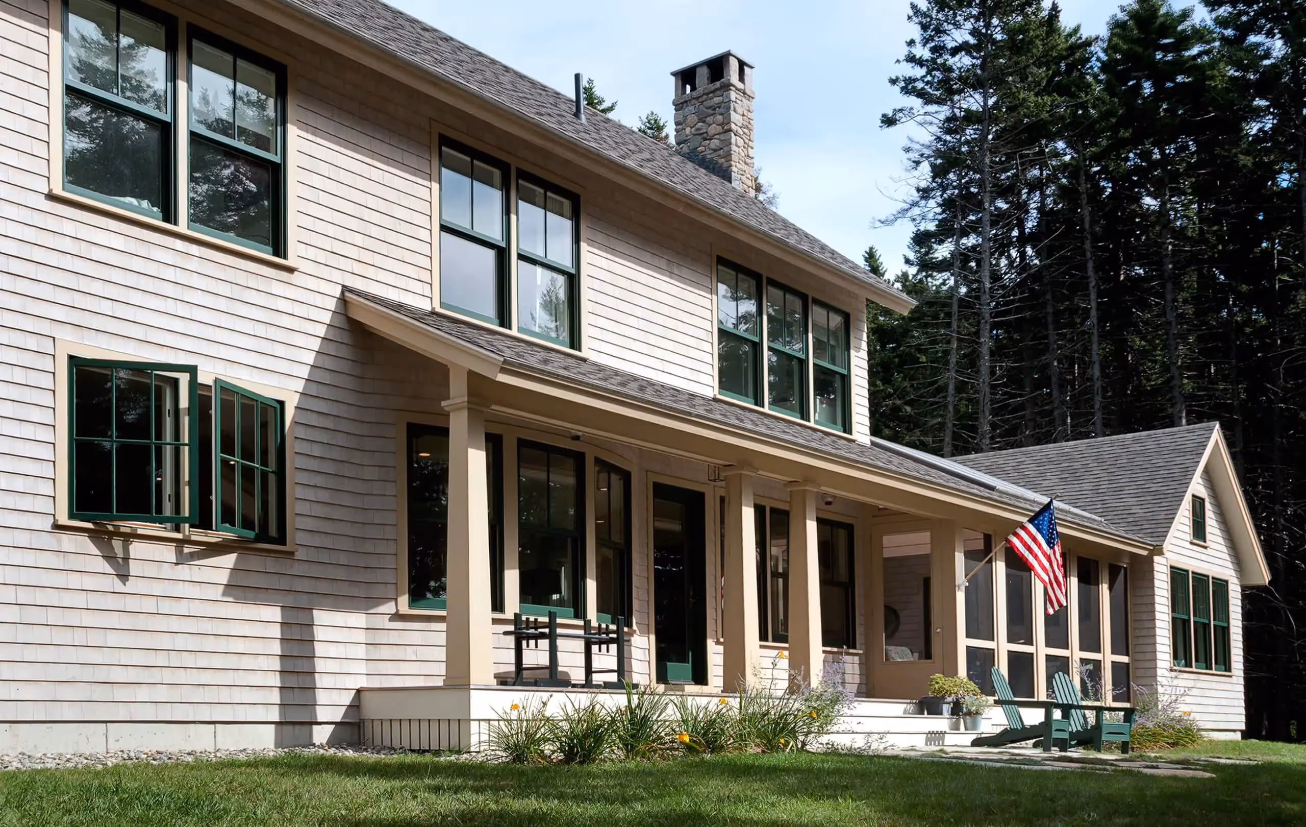 Coastal home with white siding, porch, green windows, and American flag