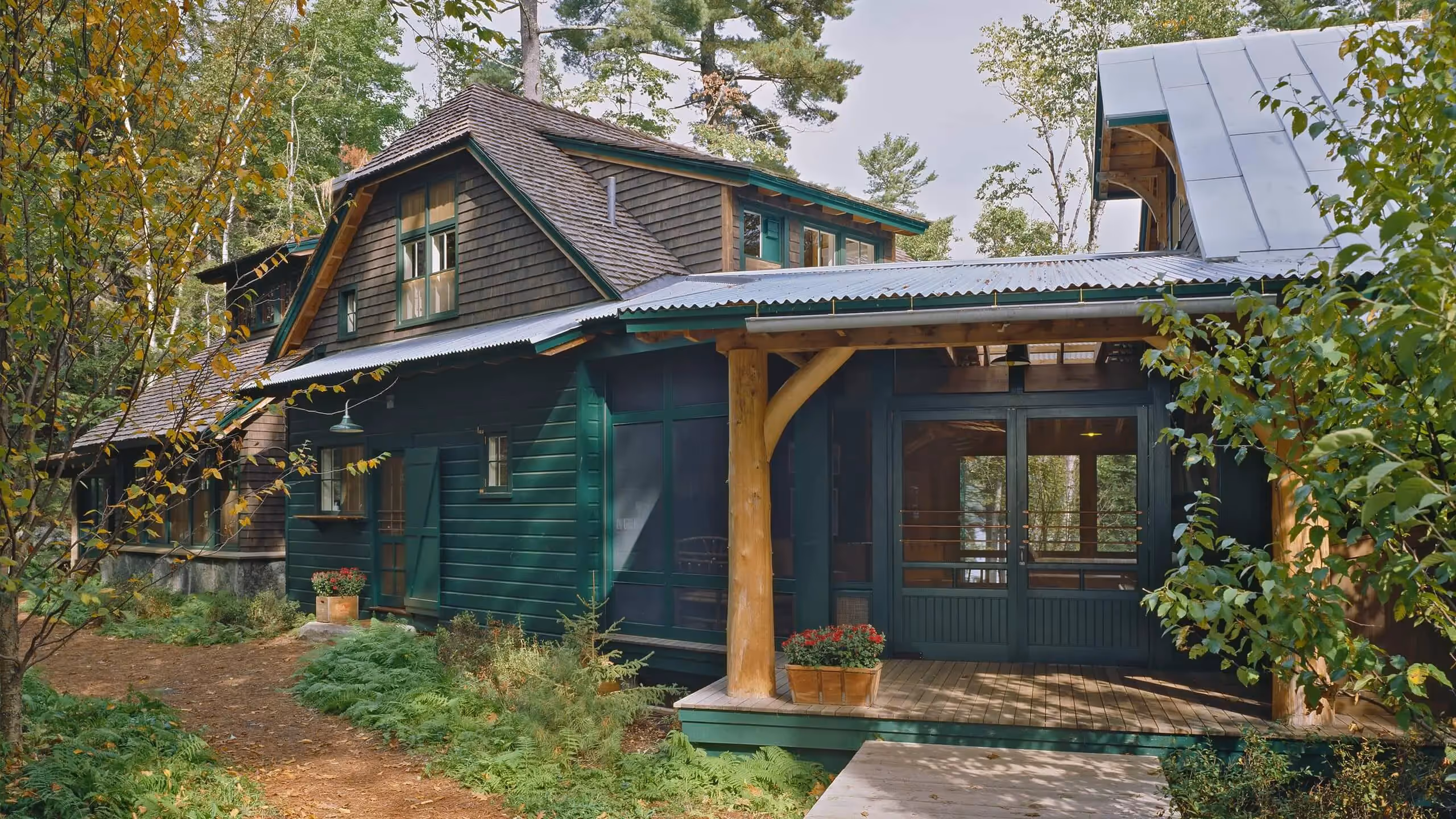 Green wooden cabin with porch nestled in lush forest surrounded by trees