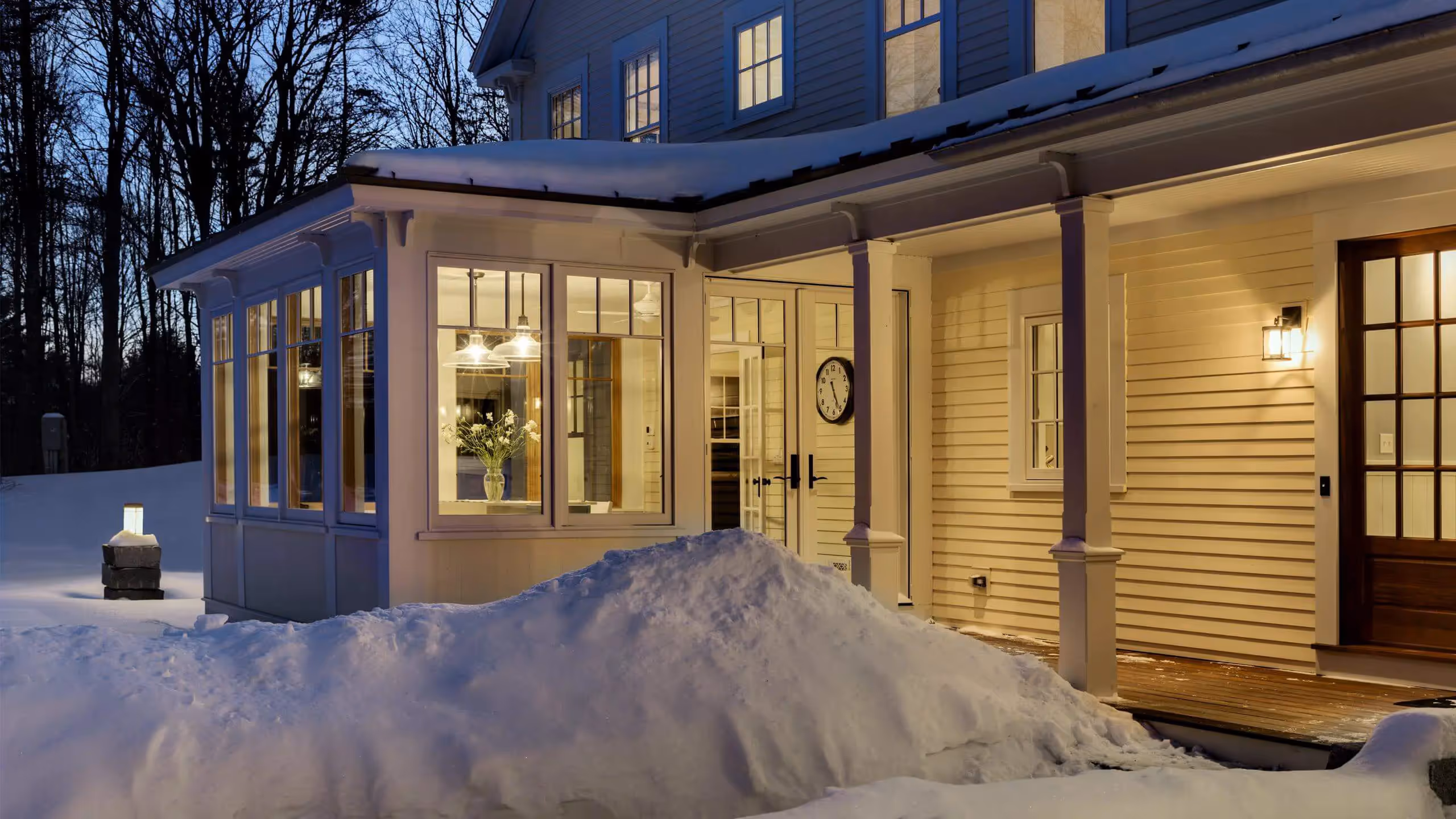Cozy winter evening, warm house lights against snowy landscape and bare trees