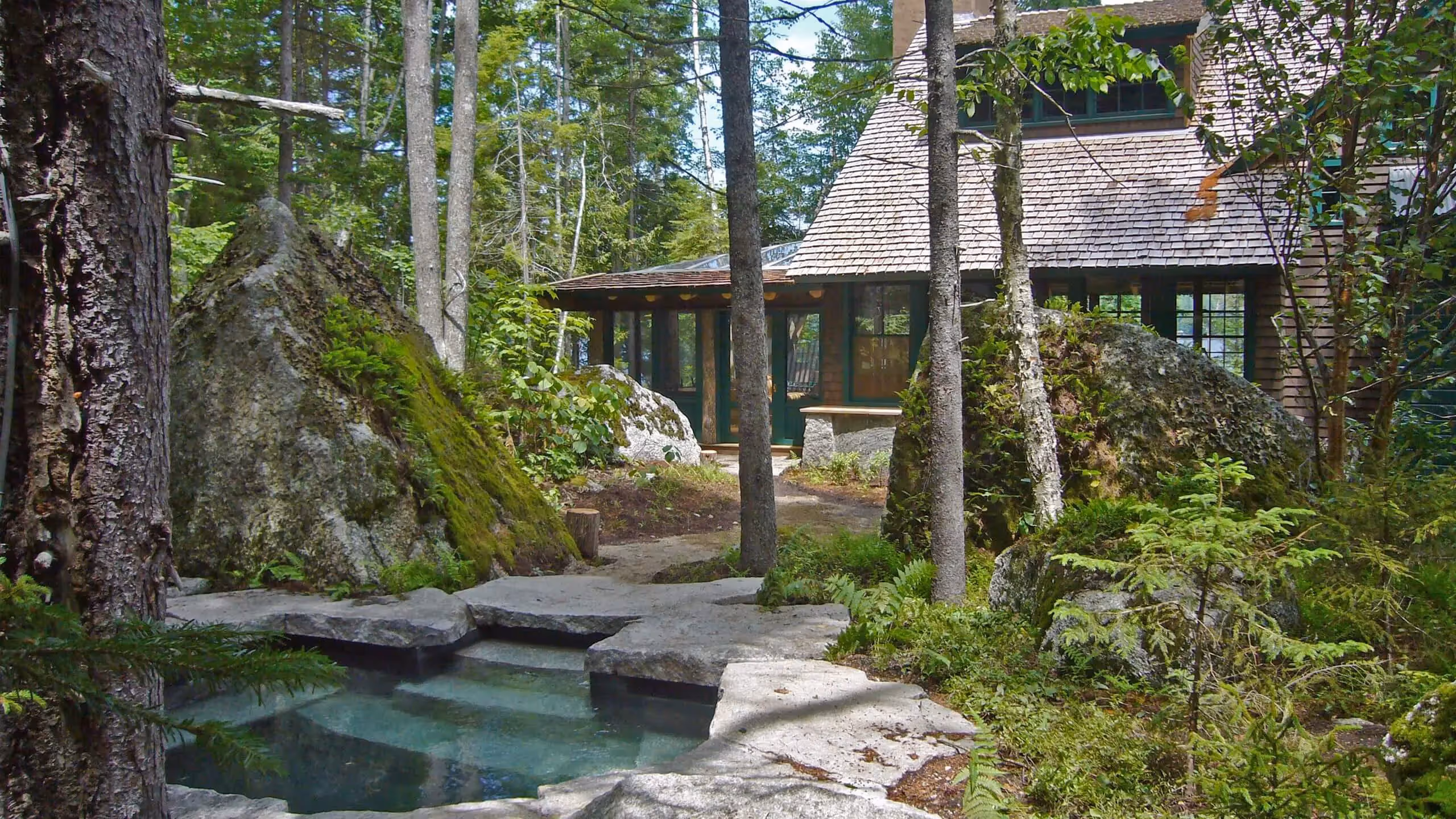 Rustic cabin nestled in forest with stone pond and mossy rocks