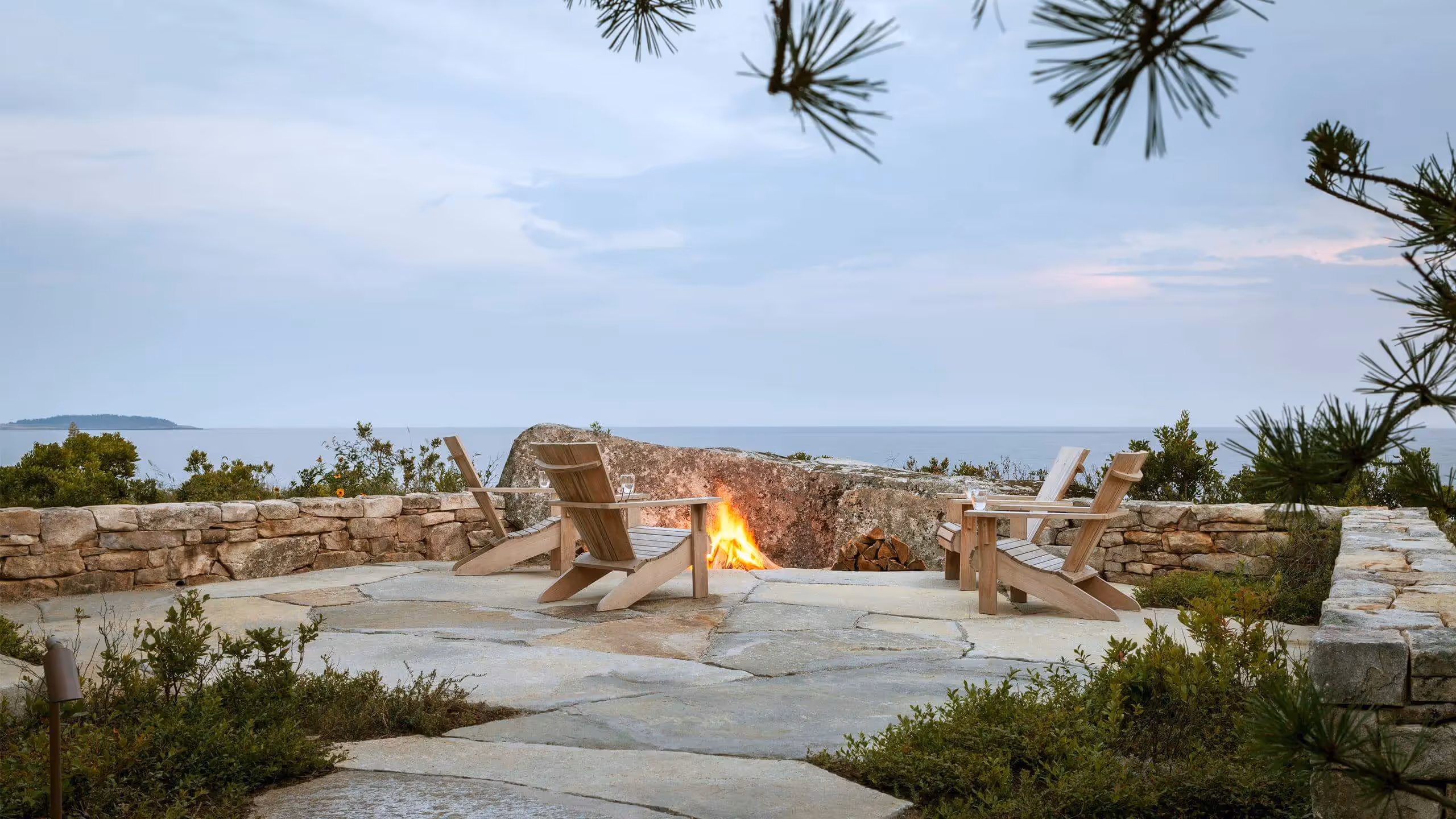 Cozy oceanside fire pit with Adirondack chairs surrounded by stone walls