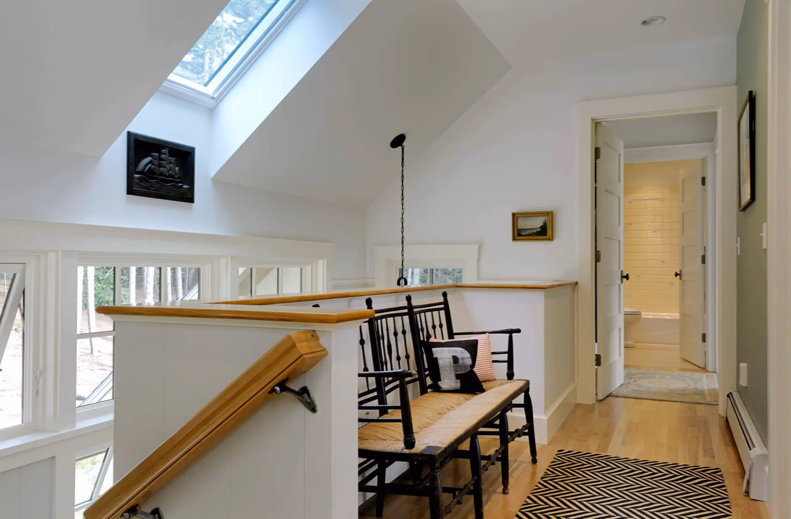 Bright attic landing with black bench, skylight, and nautical artwork