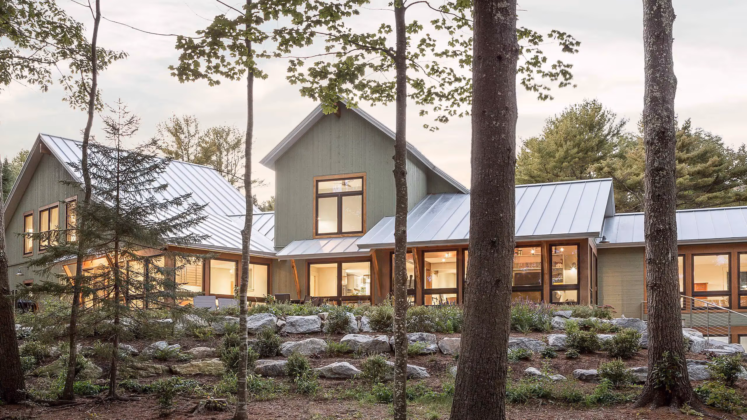 Modern green house with metal roof nestled among trees and rocks