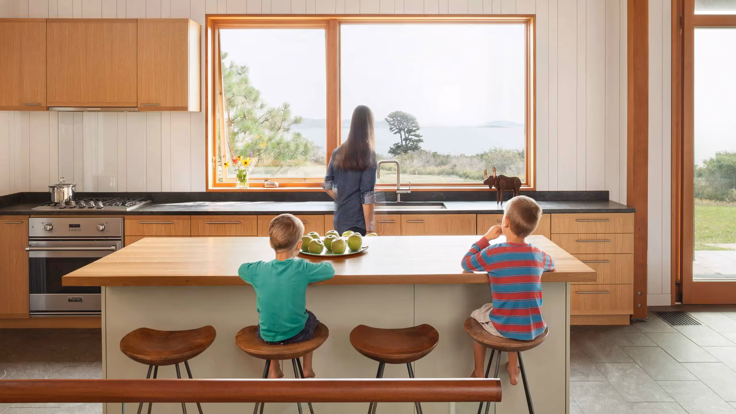 Two children sit at kitchen island, looking out window with adult