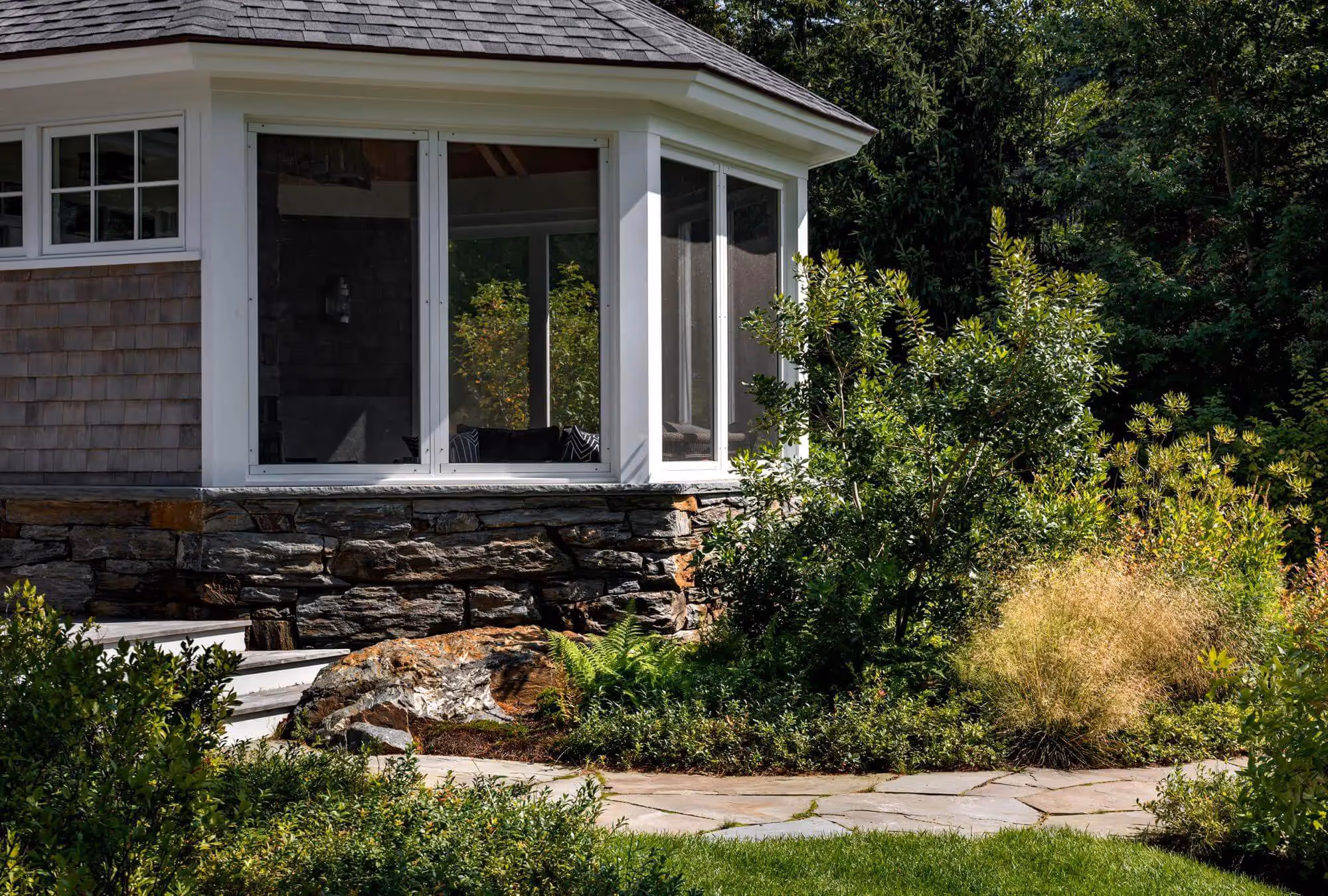 White bay window house with stone foundation and lush garden landscaping