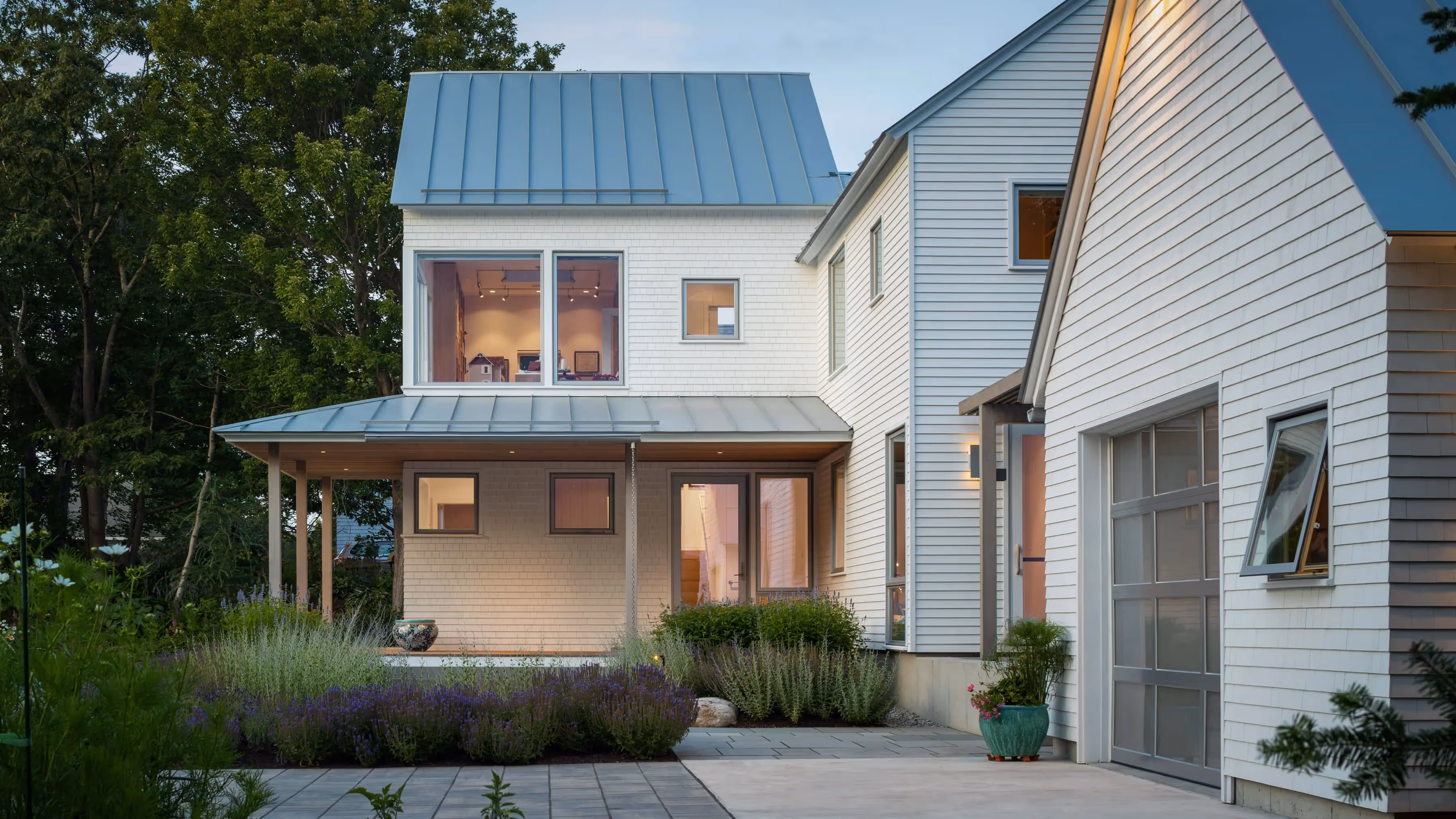 Modern white and blue house with metal roof and lavender landscaping at dusk