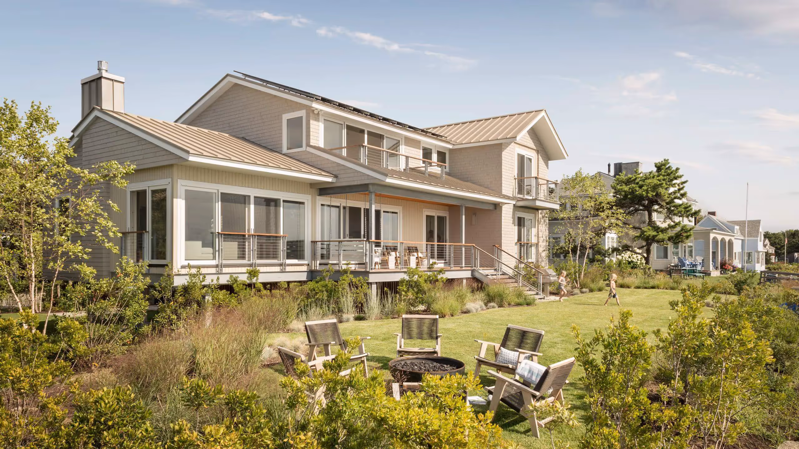 Modern beach house with deck, lawn, fire pit, and surrounding greenery