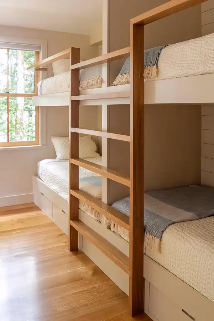 Modern wooden triple bunk bed with neutral bedding in bright room