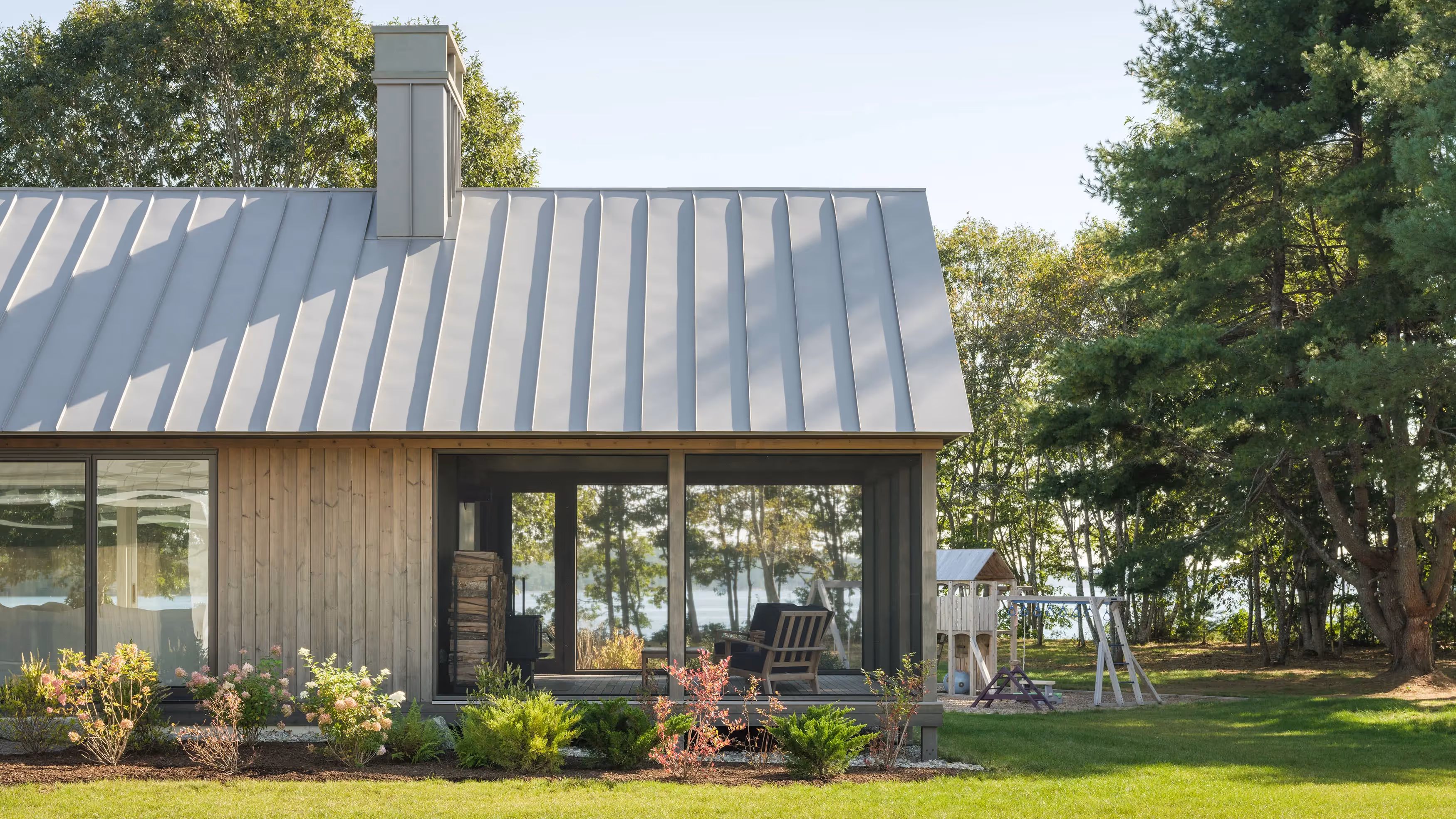 Modern cabin with metal roof and large windows overlooking water and playground