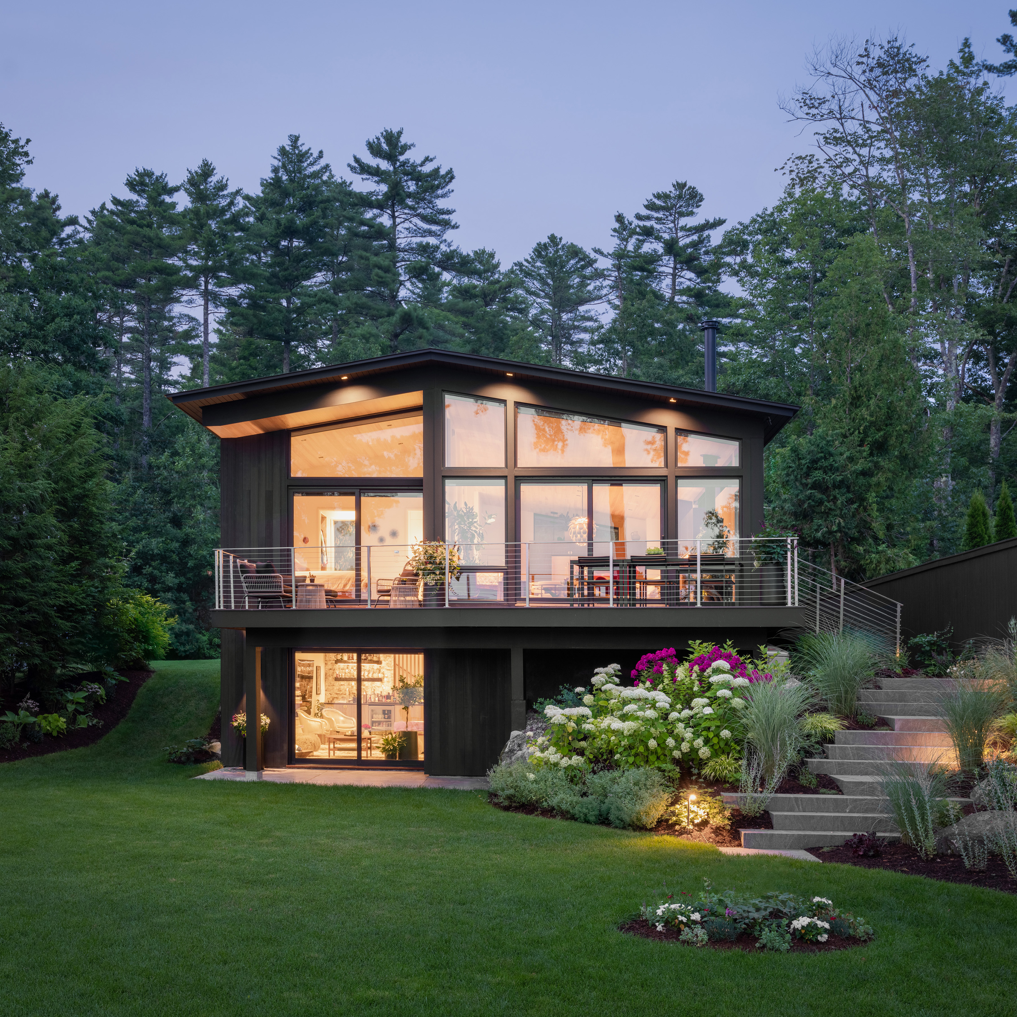 Modern two-story house with large windows nestled in pine forest at dusk