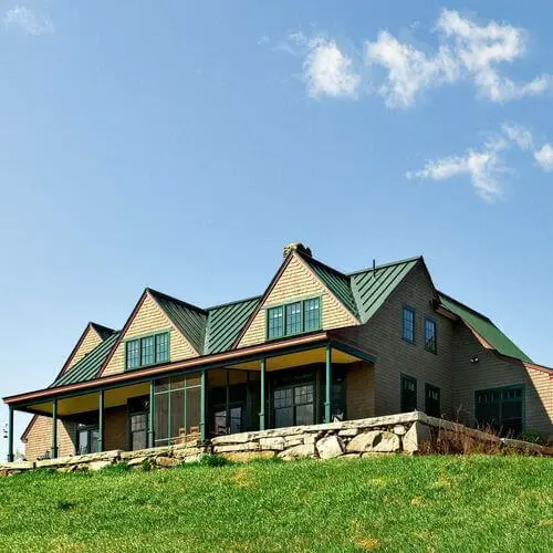 Large wooden house with green roof on grassy hill under blue sky