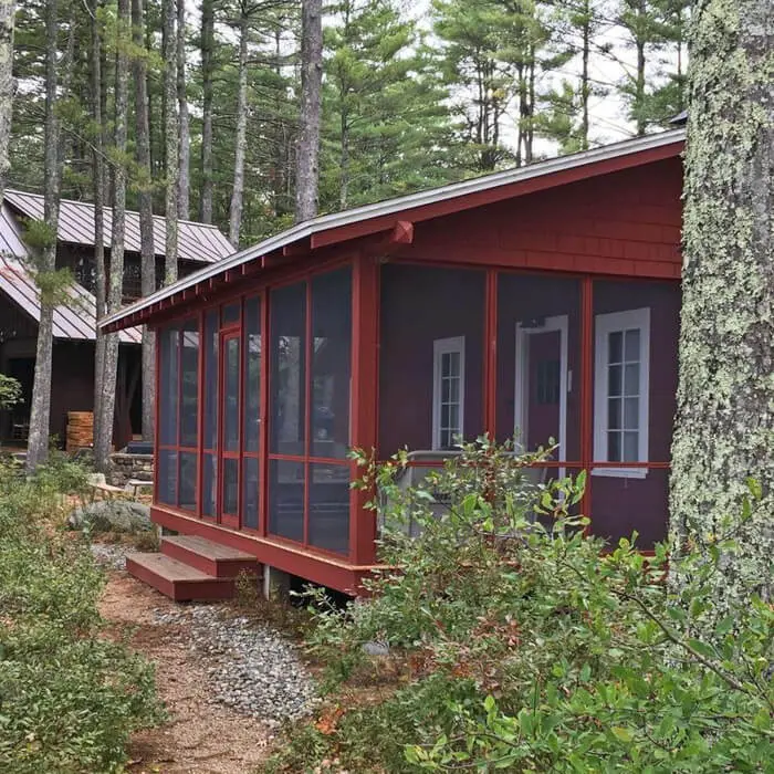 Red wooden cabin with screened porch nestled in pine forest