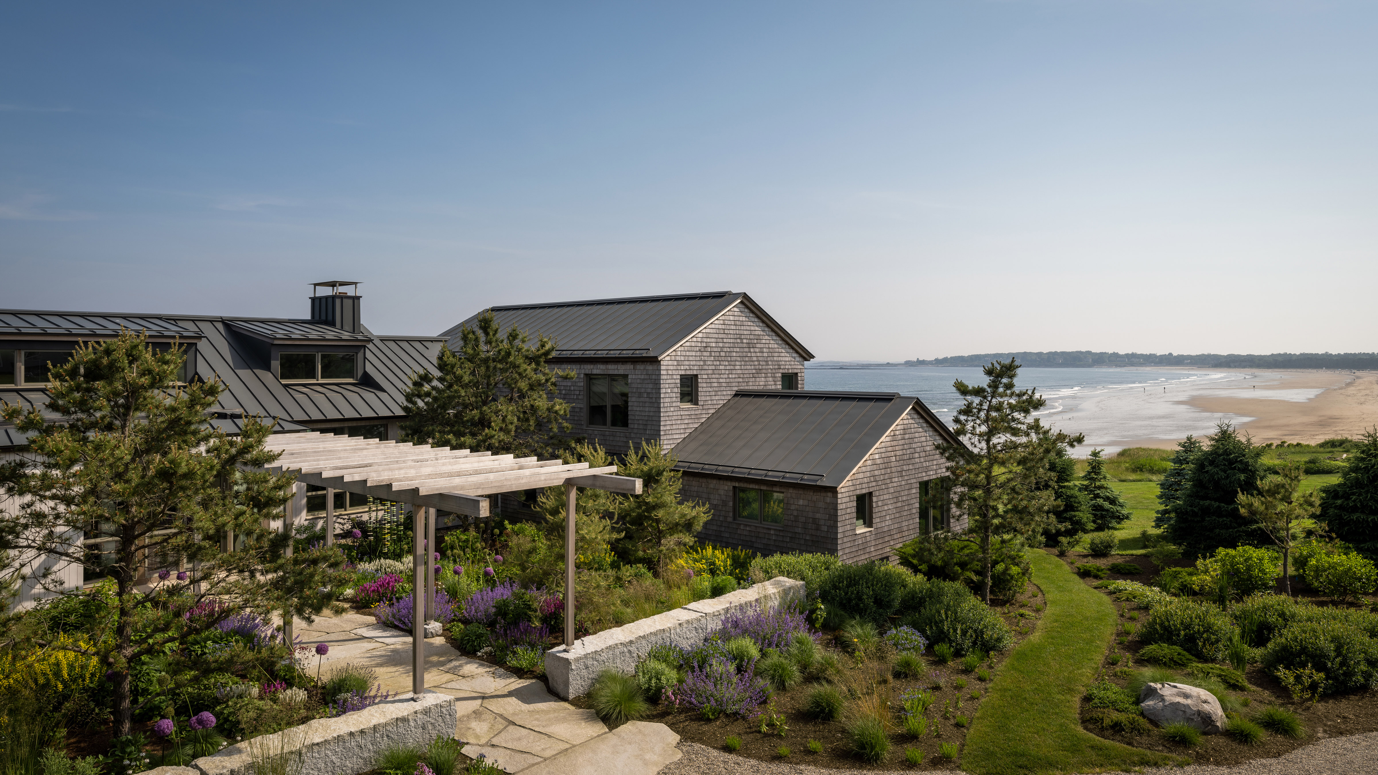 Contemporary coastal residence with cedar shingles and metal roofs on Maine coastline with ocean views, designed by Whitten Architects.