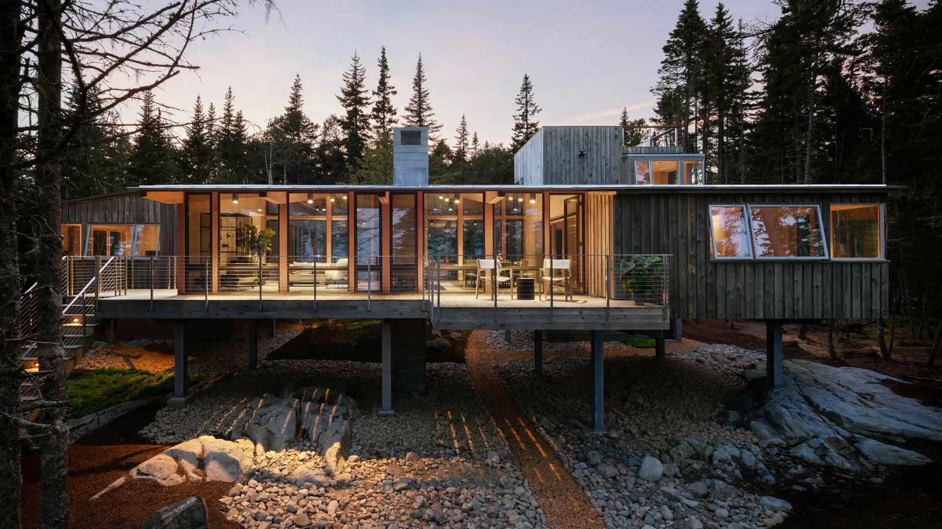 Modern wooden cabin on stilts in forest with glass walls at dusk