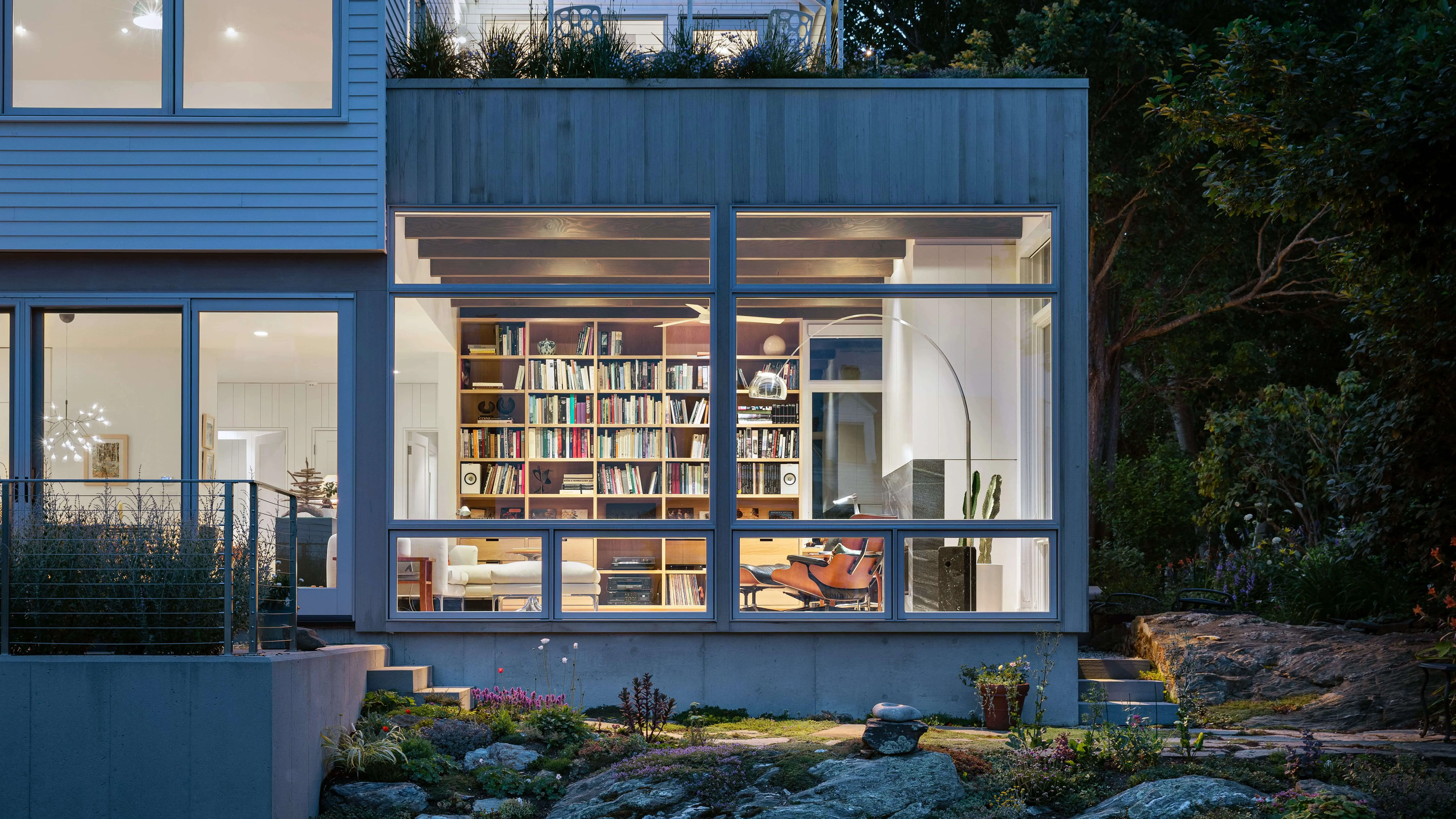 Modern blue house with large windows revealing cozy library and living space