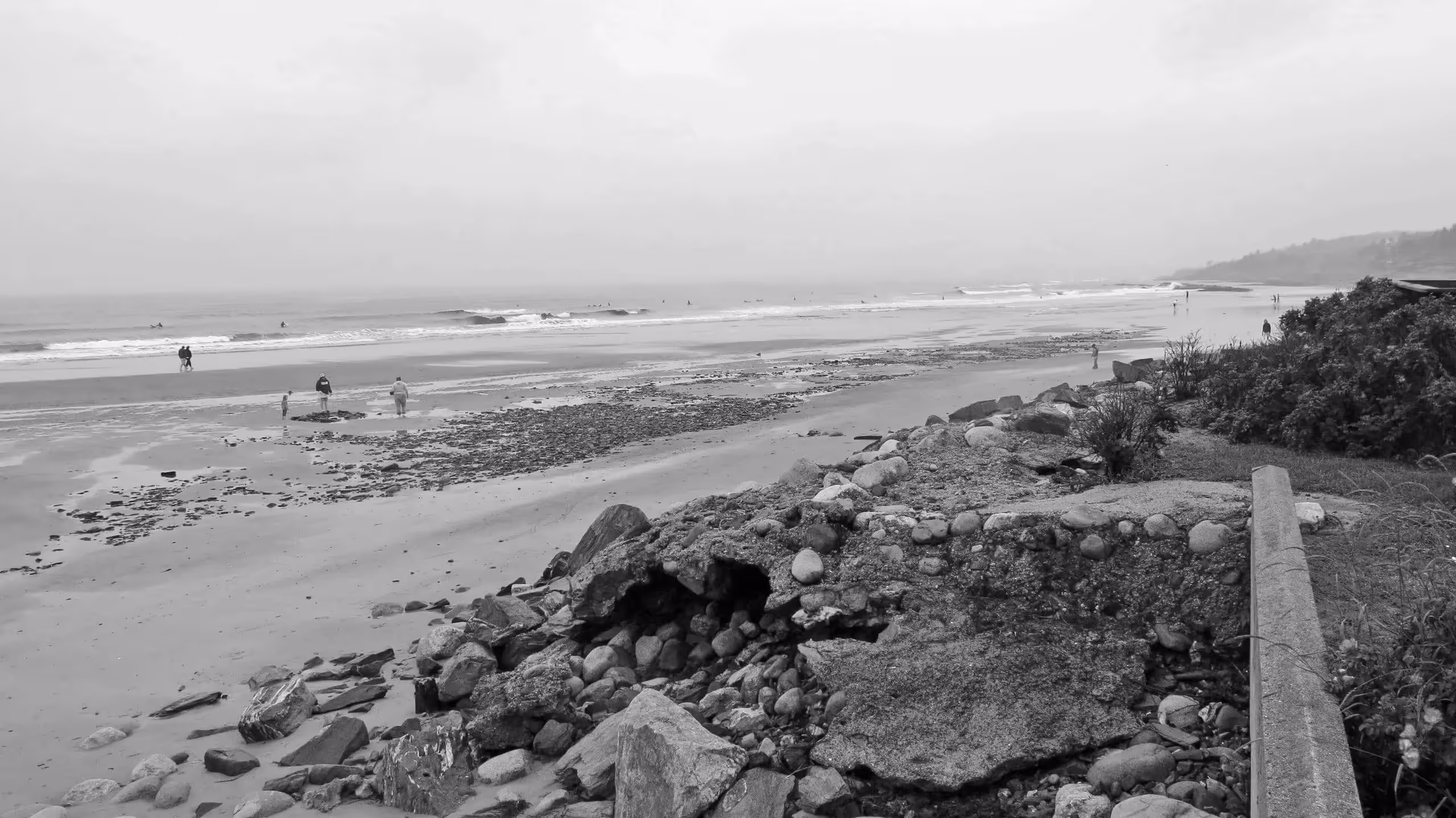 Rocky coastline with scattered people walking on a misty beach