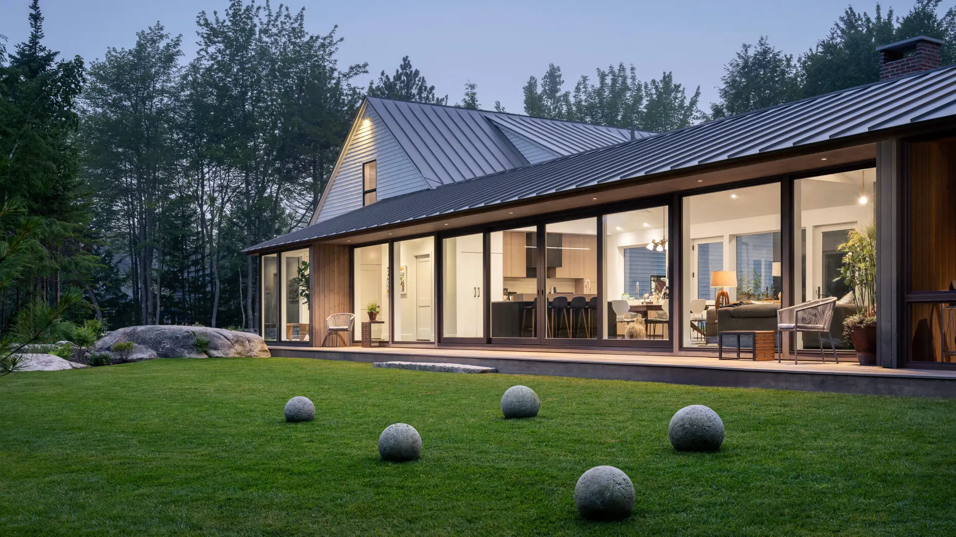 Modern house with large windows, stone spheres on lawn, surrounded by trees