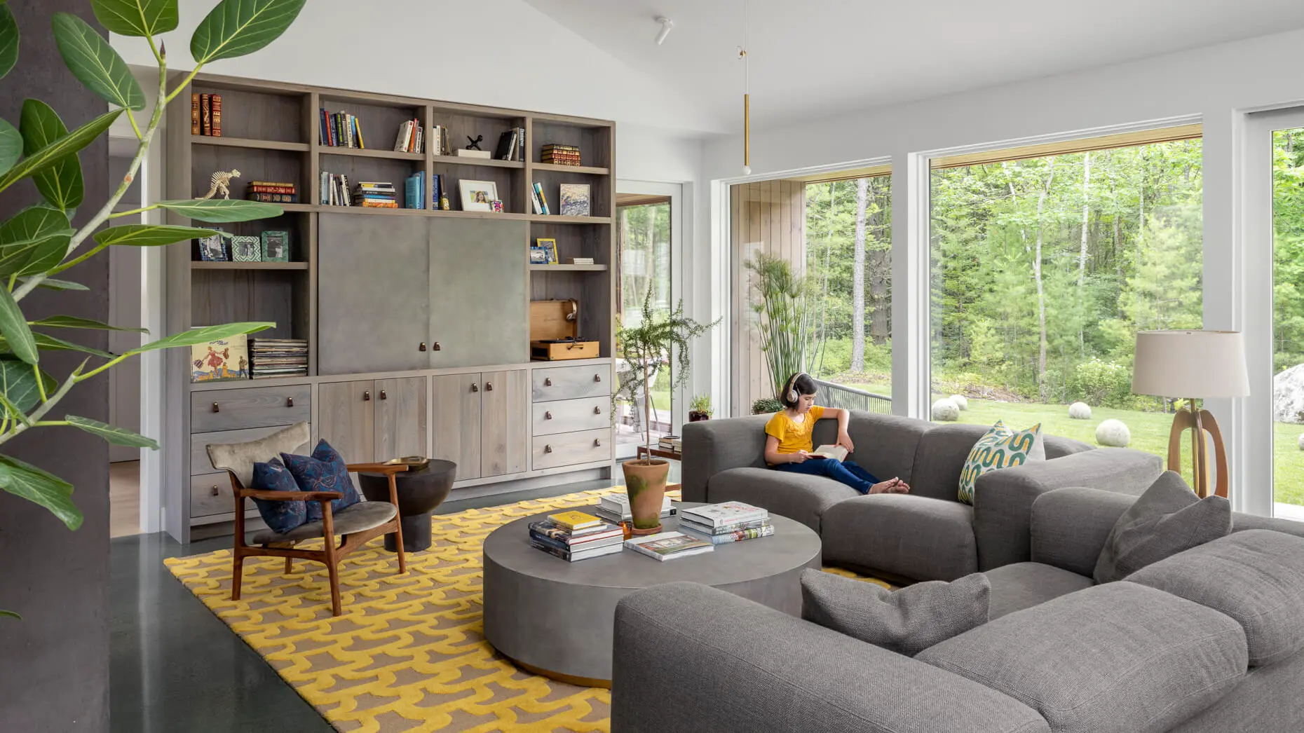 Modern living room with gray sectional, yellow rug, and forest view