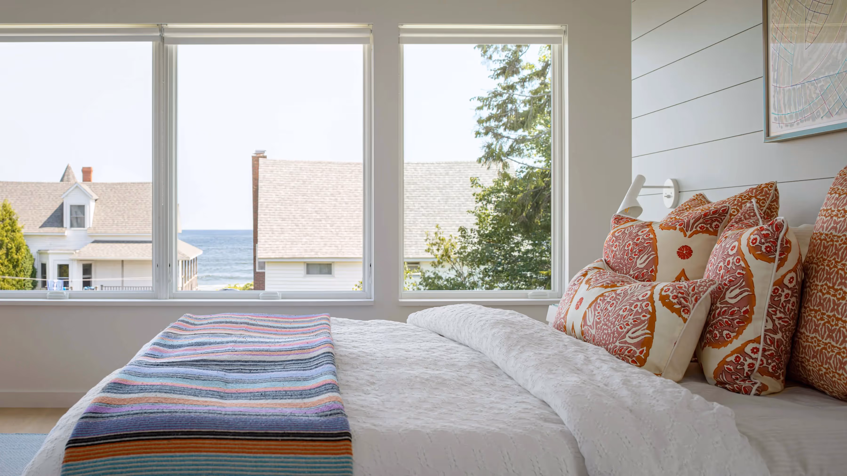 Bright bedroom with ocean view, colorful pillows, and striped blanket