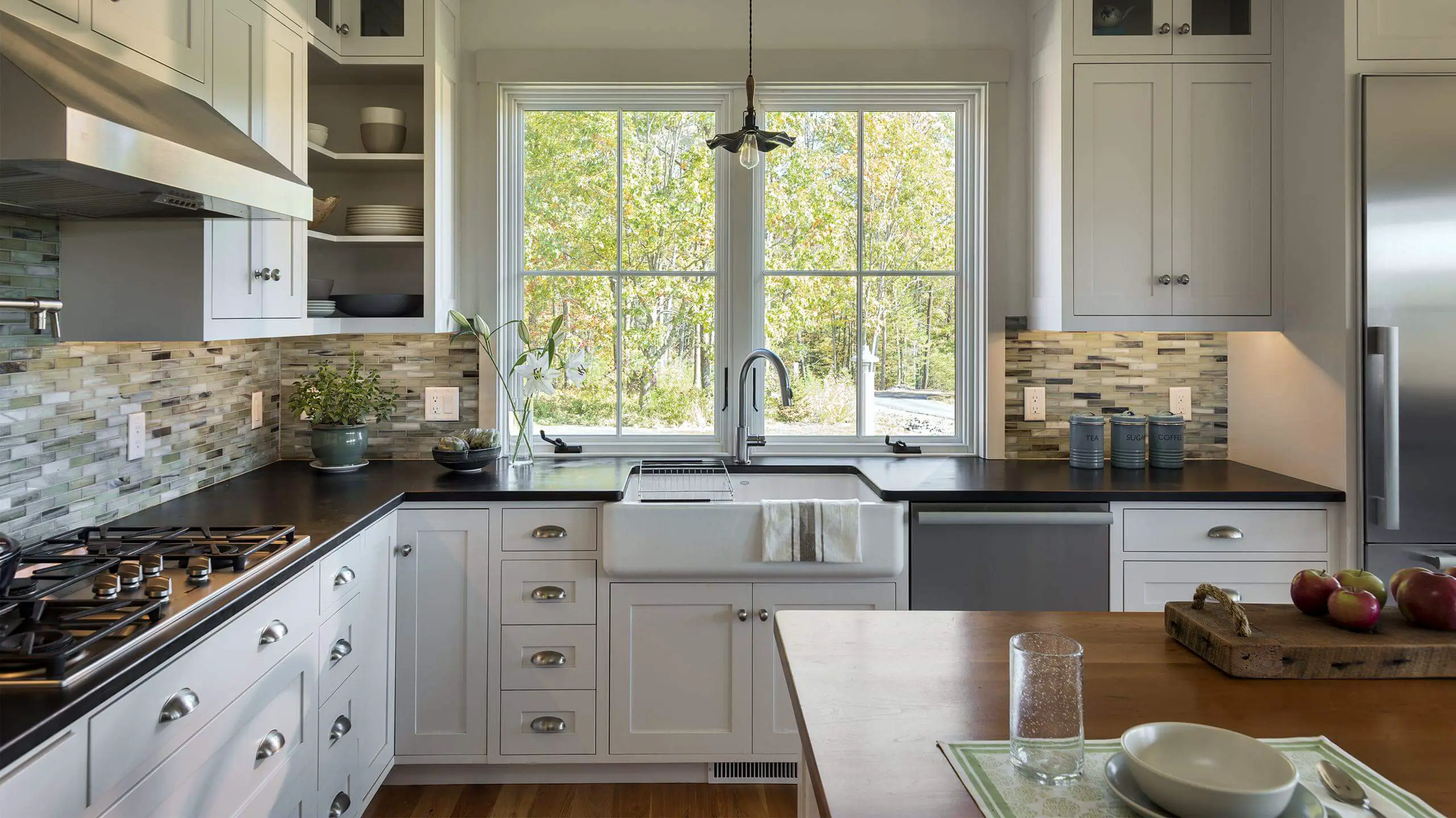 Modern white kitchen with large windows, black countertops, and natural light