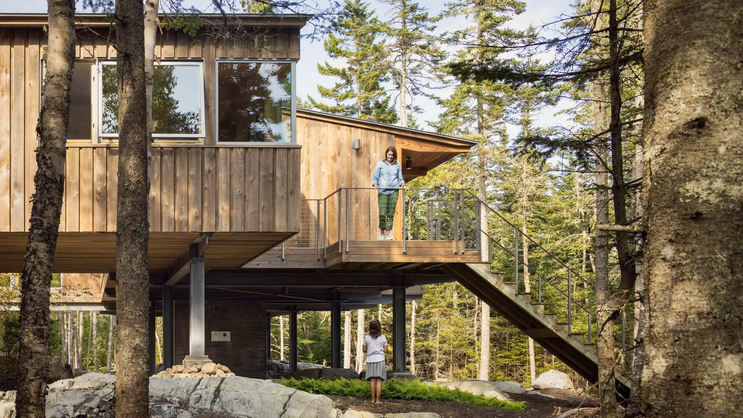 Modern wooden treehouse elevated among pine trees with two people