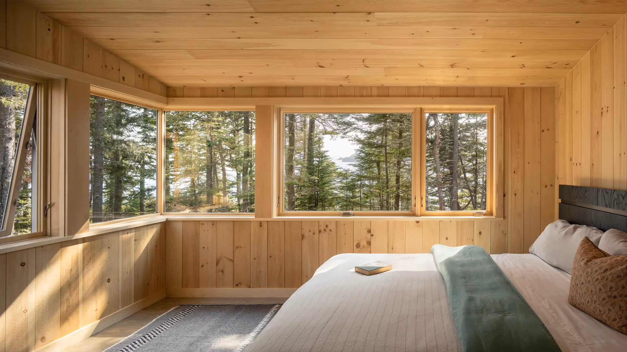 Wooden bedroom with large windows overlooking pine forest and sunlight