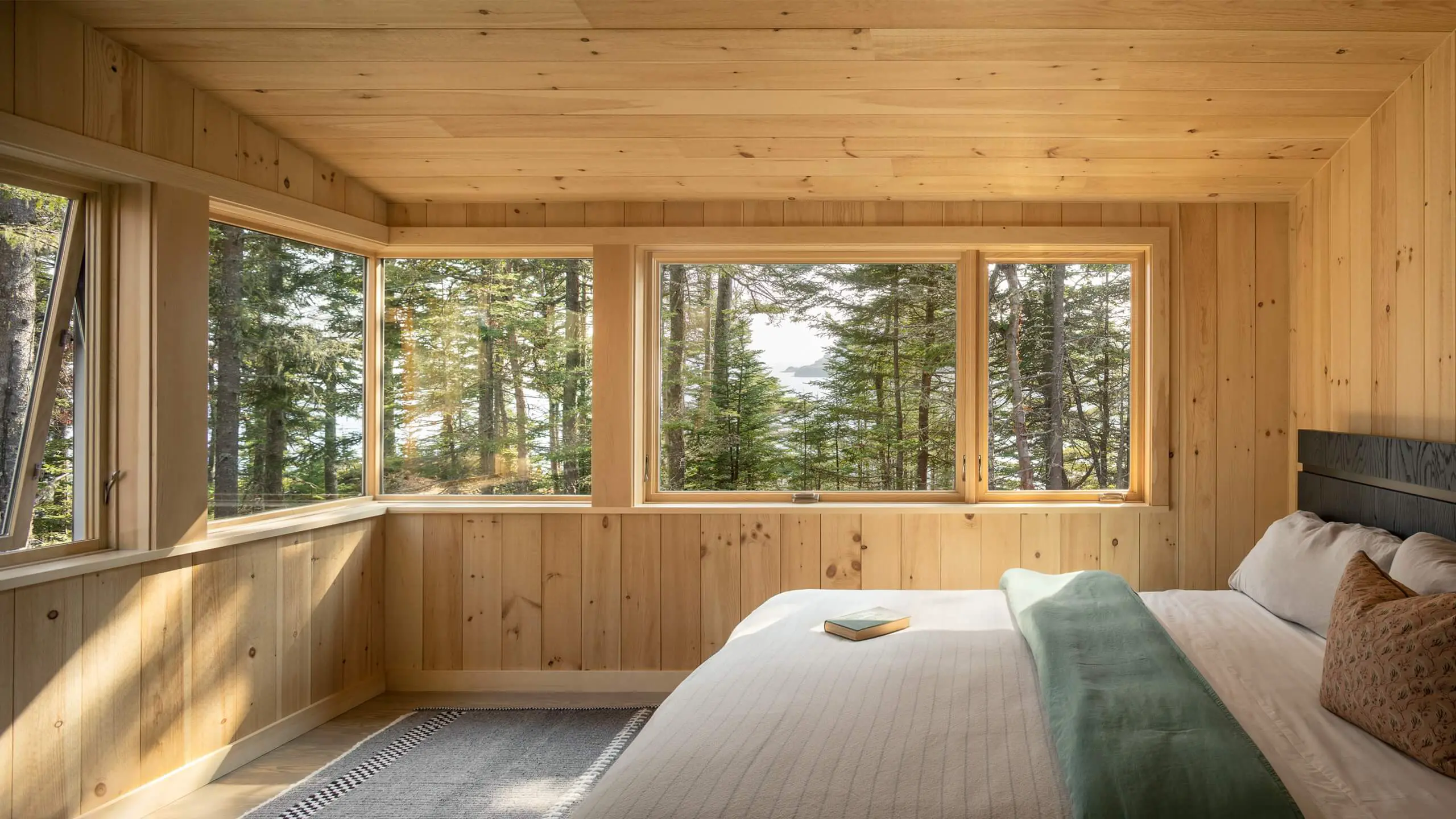 Wooden bedroom with large windows overlooking pine forest and sunlight