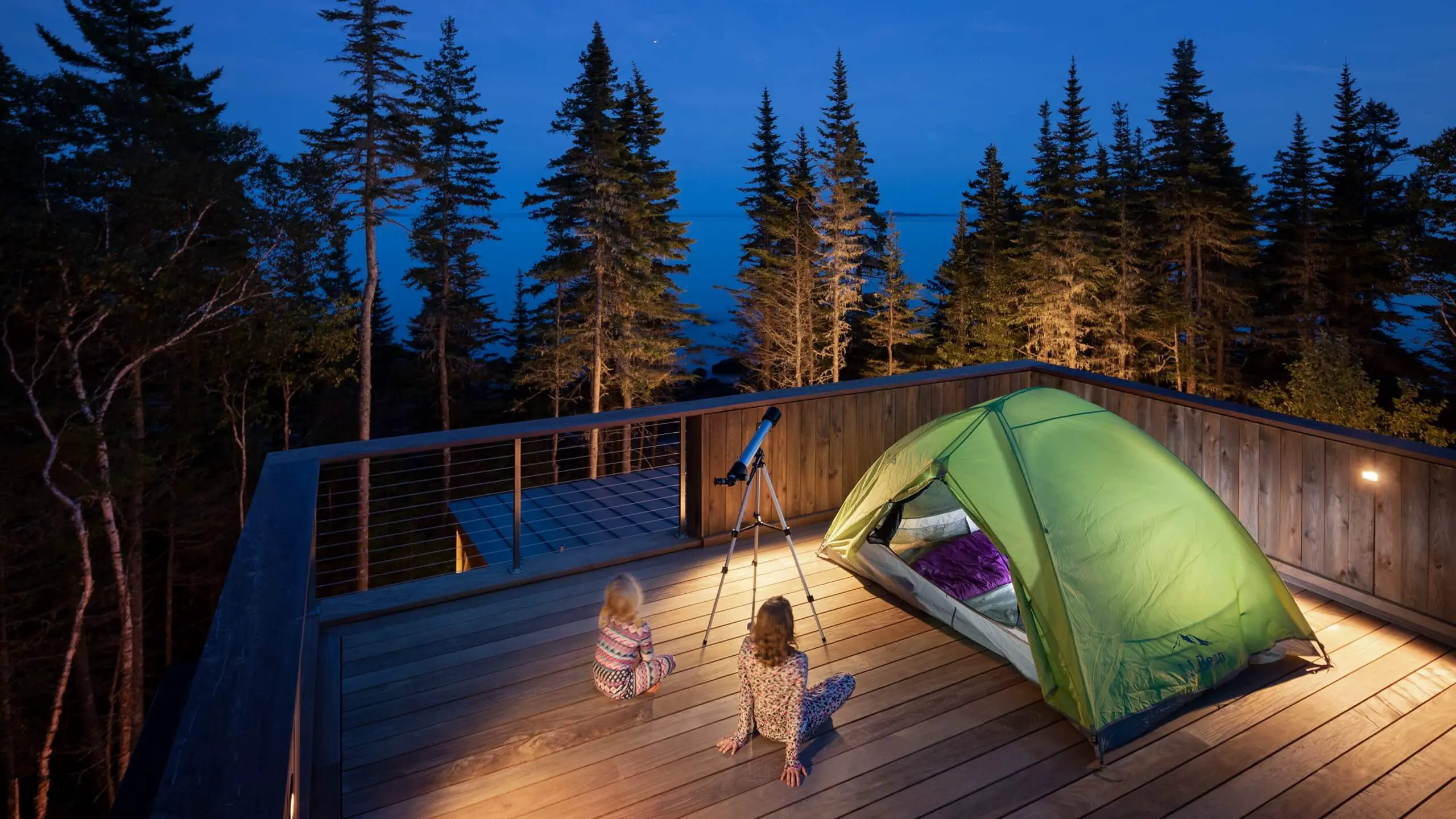 Green tent on wooden deck at night with telescope and forest backdrop