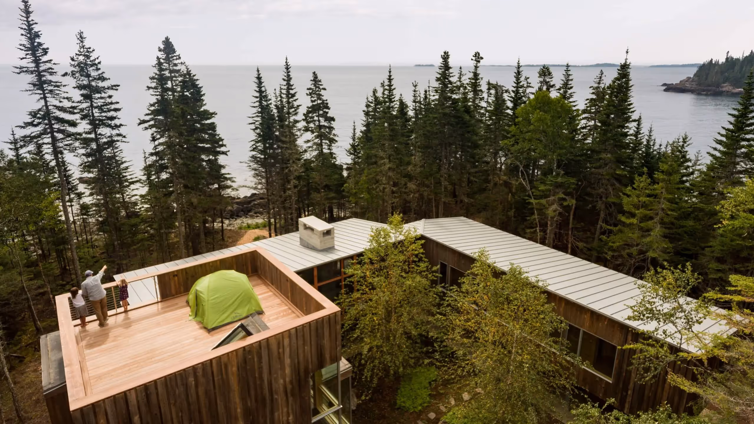 Green tent on wooden deck overlooking ocean and pine forest