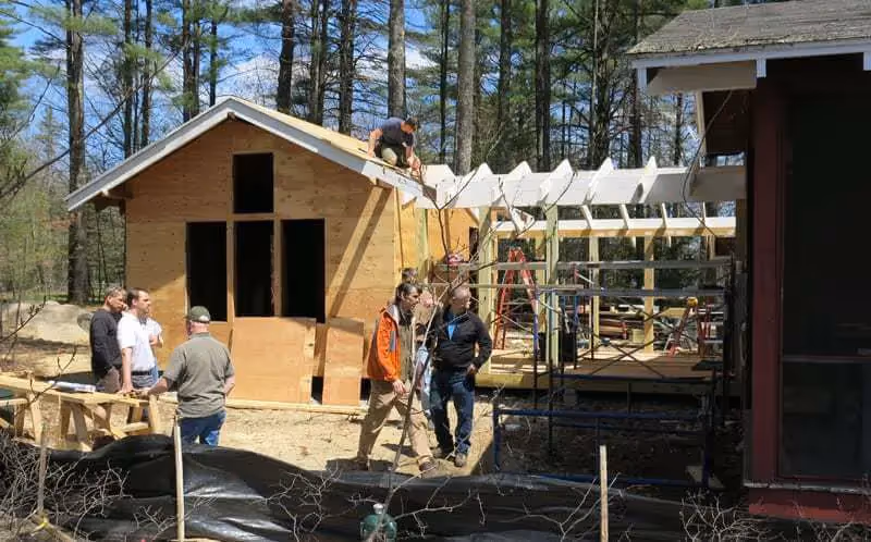 People building wooden cabin in forest with construction materials and ladders
