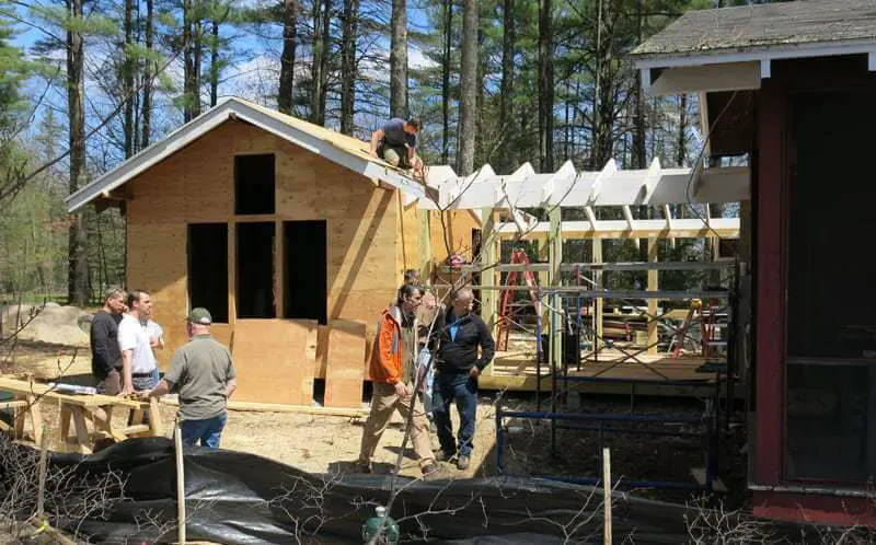 People building wooden cabin in forest with construction materials and ladders