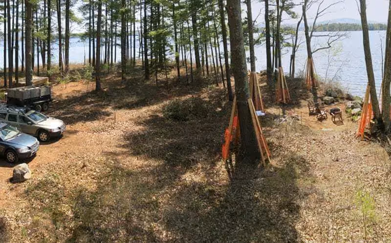 Lakeside campsite with parked SUV among pine trees and camping equipment