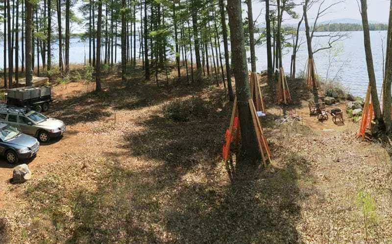 Lakeside campsite with parked SUV among pine trees and camping equipment