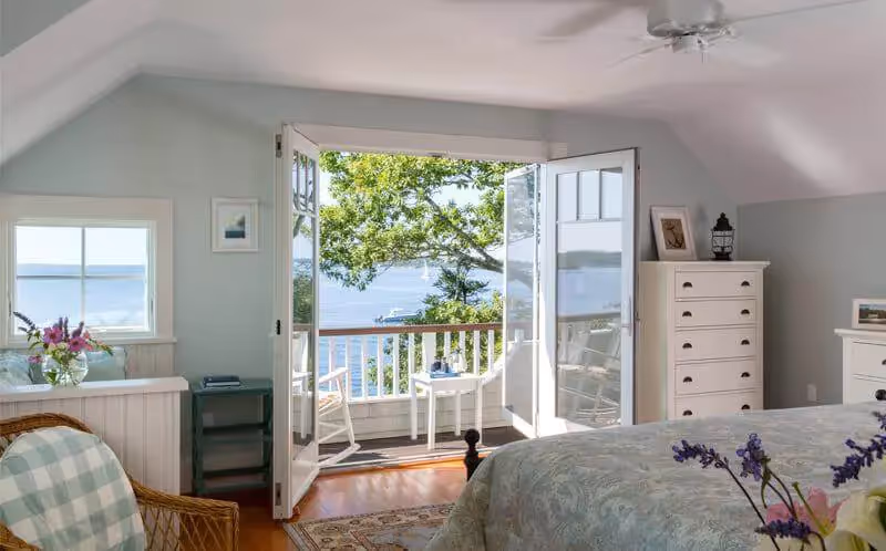 Bright coastal bedroom with open doors revealing ocean view and balcony