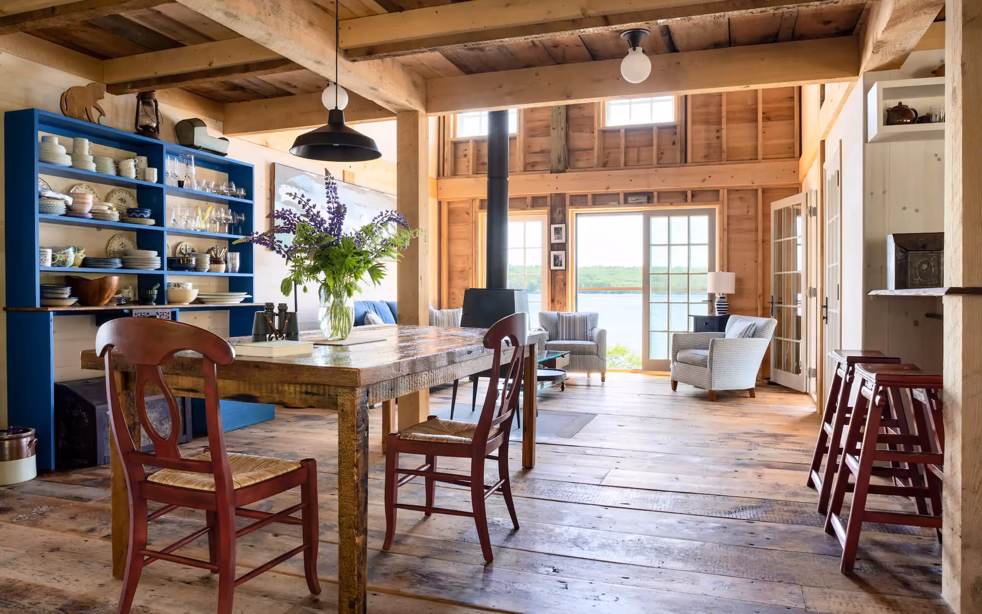 Rustic wooden dining area with blue shelves, wooden table, and large windows