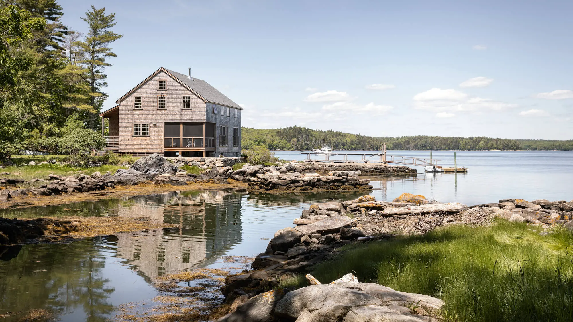 Rustic wooden cottage on rocky shore with boat dock and calm lake